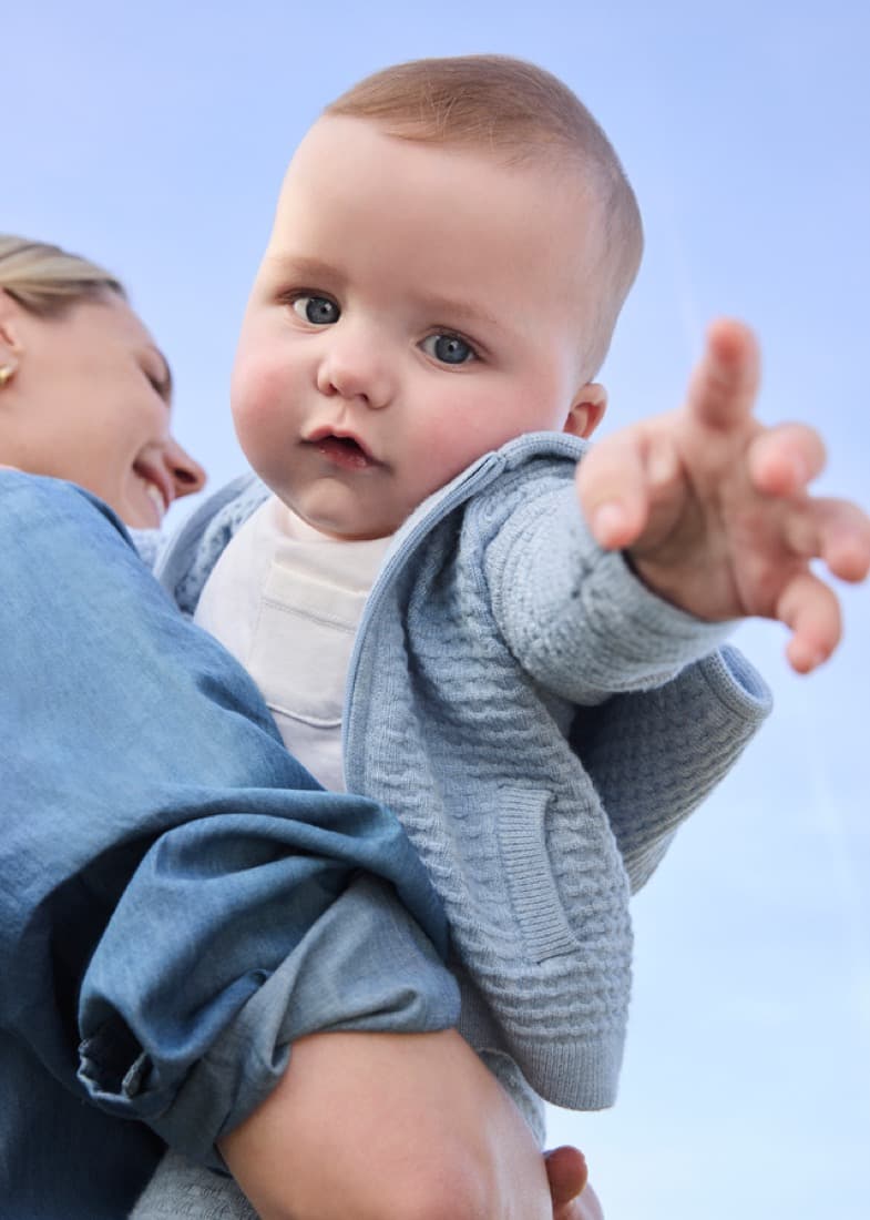 Mum lifting her baby, dressed in a blue Mayoral knitted cardigan