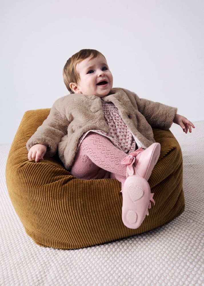 Laughing baby in a Mayoral faux-fur coat and pink tights